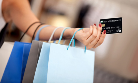 Woman holding several bags on her arm while shopping, with a credit card in hand