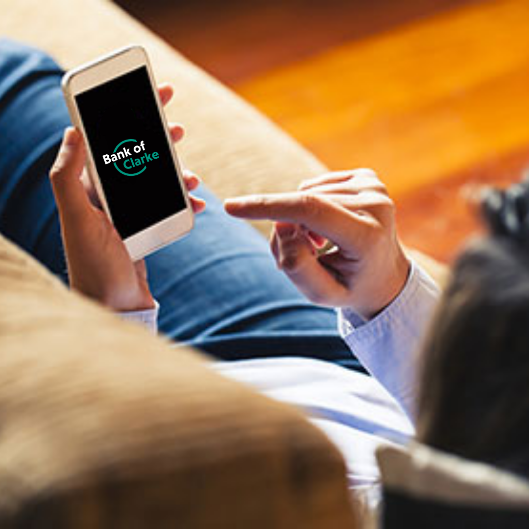 Person sitting on couch, looking at Bank of Clarke County on smartphone